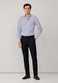 Prugasta košulja s dugim rukavima u plavoj i bijeloj boji, uparena s krojenim crnim hlačama. Odijelo ima uski kroj i minimalne detalje.