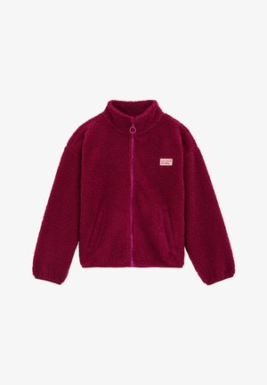Fleece bunda v magentovej farbe s vysokým golierom, predným zipsom a dvoma bočnými vreckami. Obsahuje malé nášivku na hrudi.