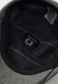 Gray wool hat interior with black and blue plaid lining, featuring a black label with "BRIXTON" logo and decorative stitch details.