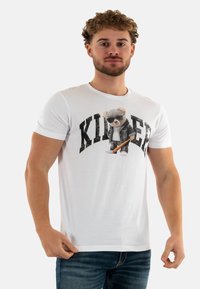 T-shirt en coton blanc avec un imprimé graphique représentant un ours portant des lunettes de soleil et une veste, avec le mot "KILLER" en lettres noires, en gras.