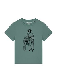 Grüne Baumwoll-T-Shirt mit einer schwarzen Illustration einer Frau, die mit einer Kuh steht und Shorts sowie einen breitrandigen Hut trägt.