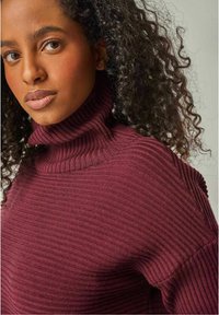 Burgunderfarbenes, geripptes Rollkragensweater mit langen Ärmeln, das ein strukturiertes Strickmuster und einen hohen, gefalteten Kragen aufweist.