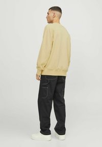 Sweat-shirt jaune clair avec des poignets et un ourlet côtelés, associé à un pantalon cargo noir avec de grandes poches et des coutures blanches, porté avec des baskets blanches.