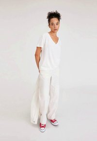 White V-neck t-shirt paired with white wide-leg pants. The outfit is complemented by red low-top sneakers. Smooth, soft fabric with minimal design.