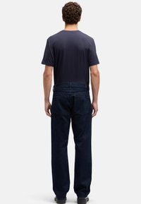 Męskie ciemnoniebieskie dżinsy i granatowy t-shirt, widoczne od tyłu, o luźnym kroju z dwoma tylniymi kieszeniami.