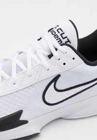 Baskets blanches de sport avec une tige en mesh, accents noirs, col rembourré et logo Nike en évidence. Semelle en caoutchouc avec un design texturé.