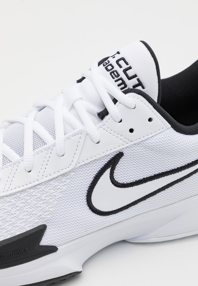 Białe obuwie sportowe z siateczkową cholewką, czarnymi akcentami, wyściełanym kołnierzem i wyróżniającym się logo Nike. Gumowa podeszwa z teksturowanym wzorem.