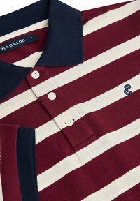 Röd och vit randig polo skjorta med marinblå krage, tre knappar och en liten broderad logotyp på bröstet. Texturerat tyg.