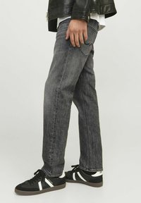 Jean en denim gris avec une coupe droite, présentant un léger délavage et des poches arrière classiques, associés à des baskets noires et une veste en cuir.