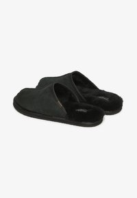 Zapatillas de ante negro con un suave forro de piel de borrego negra, diseño tipo slam y suelas de goma blandas. Presentan costuras sutiles y un perfil bajo.