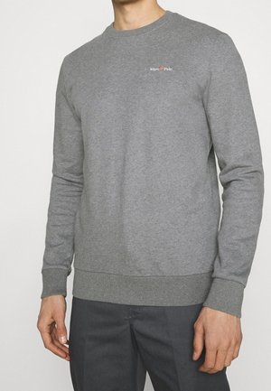 Man draagt een effen grijze trui met ronde hals met een klein "Marc O'Polo"-logo op de borst en donkere grijze broek, staand tegen een witte achtergrond.