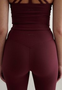 Burgundowy zestaw odzieży sportowej charakteryzuje się prążkowaną strukturą. Top ma wąskie ramiączka, a legginsy o wysokim stanie mają logo i bezszwowy design.