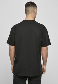 Črn bombažni majica s kratkimi rokavi in sproščenim krojem. Nazaj je gladka površina z minimalnimi šivi in zaobljenim izrezom.