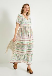 Robe maxi en tissu léger avec des motifs rayés verts, violets et rouges. Dotée d'un col en V, d'une taille à nouer et de manches courtes ; associée à des sabots marron.