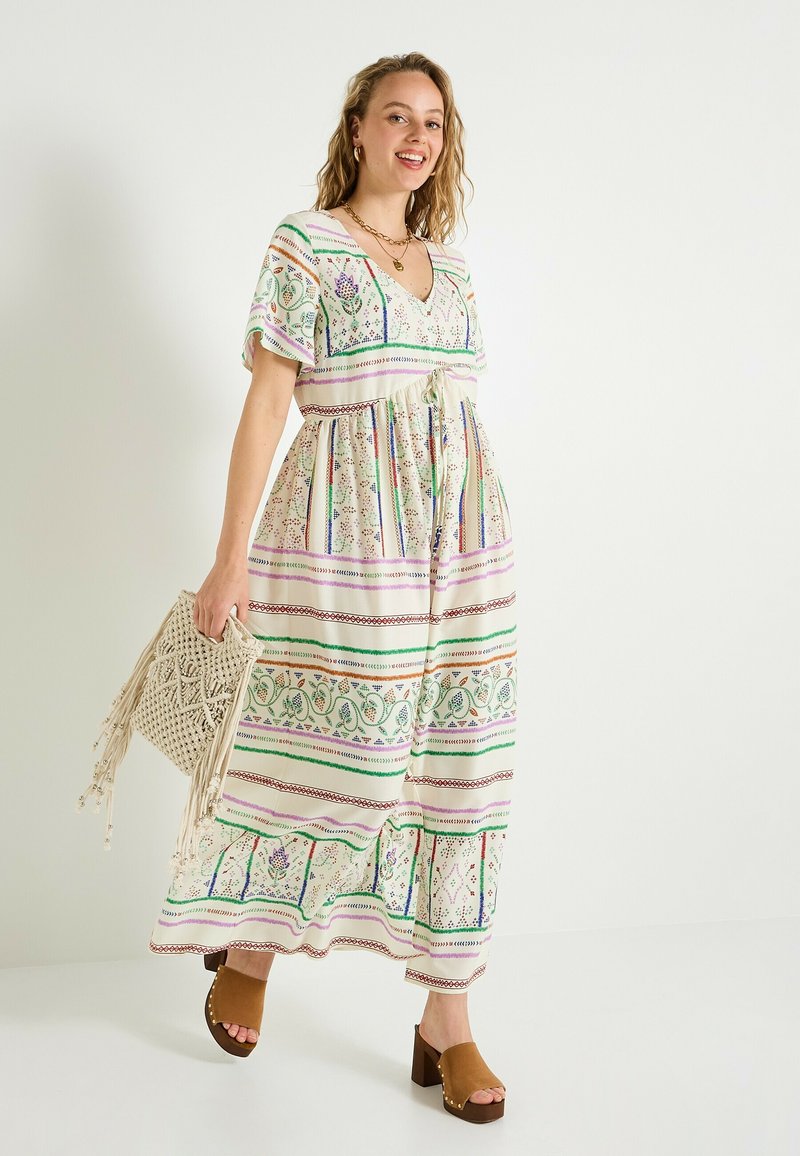 Vestido maxi de tela ligera con patrones de rayas en verde, púrpura y rojo. Presenta un escote en V, cinturilla con lazo y mangas cortas; combinado con zuecos marrones.