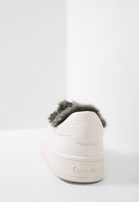 Sneaker bianco in ecopelle con trim in pelliccia grigia sul retro, caratterizzato da una suola in gomma testurizzata e logo Calvin Klein in rilievo sul tallone.