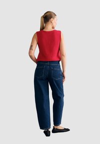 Czerwona bezrękawnikowa bluzka dzianinowa w połączeniu z niebieskimi dżinsami o wysokim stanie. Czarne baletki z siateczki. Prosta fryzura i geometryczne kolczyki.