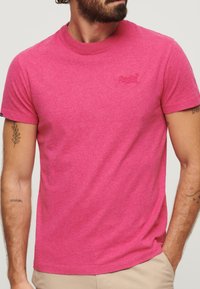 T-shirt a maniche corte e collo rotondo di un brillante colore rosa, realizzato in tessuto morbido; presenta un piccolo logo ricamato sul petto.