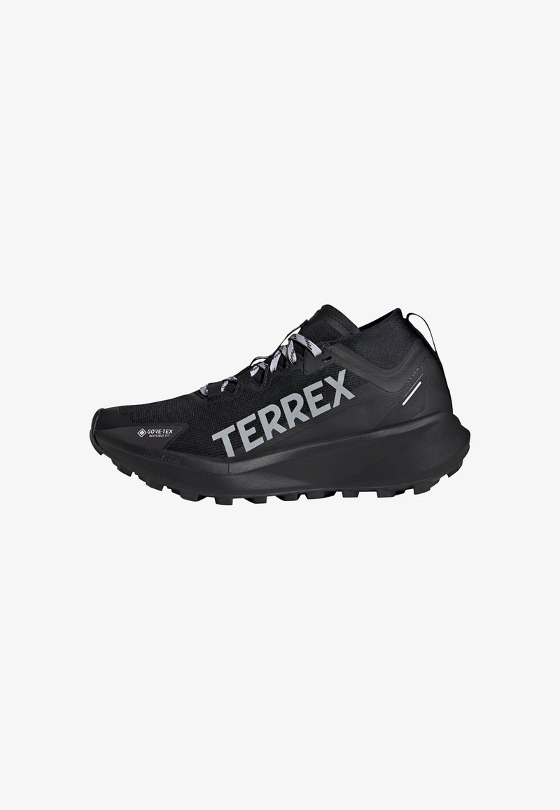 Zwarte sportieve schoen met een gestructureerde bovenkant, voorzien van "TERREX" branding, vetersluiting en een robuuste buitenzool voor grip.