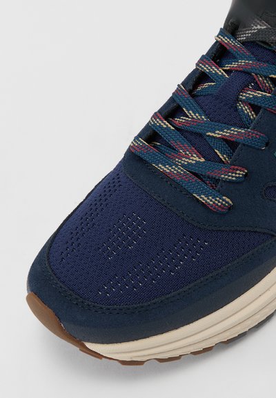 Baskets bleu marine avec tissu texturé, sections perforées et lacets multicolores. Dotées d'une semelle rembourrée avec un profil de couleur brun clair.