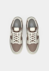 Nike tenisice imaju bež i smešnu paletu boja s glatkim koženim i mrežastim dizajnom, okruglim vrhom i tradicionalnim vezanjem na vezice.