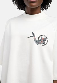 Oversized witte katoenen t-shirt met een kleurrijke koi vis afbeelding gedrukt aan de linkerkant, met korte mouwen en een hoge halslijn.
