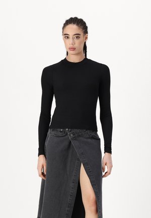 Svart langermet topp laget av glatt stoff, kombinert med en grå denim omslagskjørt med høy splitt og to frontlommer.