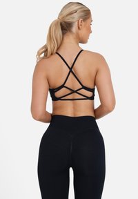 Top sportivo nero con spalline incrociate e leggings neri a vita alta, caratterizzati da una texture liscia e un design aderente, visti da dietro.
