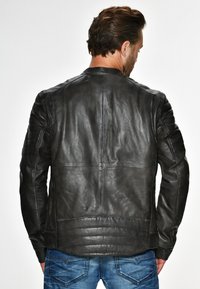 Schwarze Lederjacke mit glatter Textur, mit gesteppten Schultern und geradem Schnitt. Genähte Teile schaffen ein strukturiertes Design.