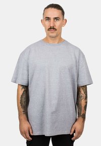 Grijze T-shirt met korte mouwen, rond de hals, een relaxte pasvorm en een gladde textuur. Het model toont zichtbare tatoeages op beide armen.