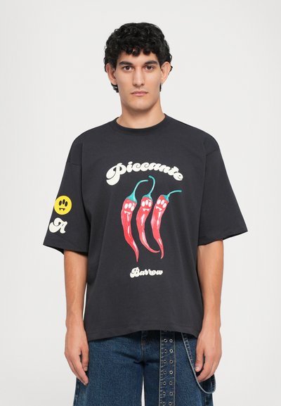 Čierne oversized tričko s grafikou červených chili papričiek a textom "Piccante Barrow". Žltá usmiata grafika na ľavom rukáve. Bavlnený materiál.