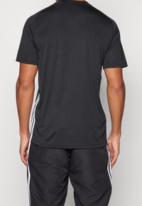 Svart idrottströja med korta ärmar, rund halsringning och vita sidestreck. Tillverkad av lätt, fukttransporterande tyg.