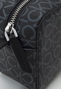 Borsa nera con texture e motivo logo a contrasto, cerniera argentata e dettagli in pelle. Forma rettangolare compatta con finitura liscia.