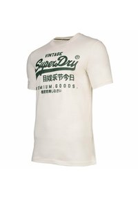 Camiseta de algodón blanca con mangas cortas, que presenta texto en verde oscuro que dice “Vintage SuperDry” y gráficos adicionales en varios estilos.
