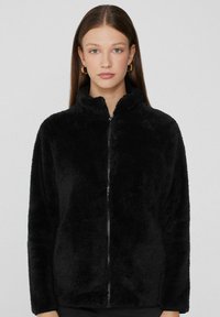 Czarna polarowa kurtka z wysokim kołnierzem, z pełnym zamkiem błyskawicznym z przodu. Materiał jest miękki i strukturalny, odpowiedni do noszenia na co dzień.
