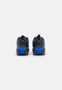 Scarpe atletiche nere e blu con tomaia testurizzata, logo giallo, linguetta e un design unico della suola, dotate di elementi di ammortizzazione.