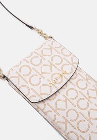 Borsa a tracolla Calvin Klein realizzata in materiale beige testurizzato, con logo dorato e motivo ripetitivo "CK", impreziosita da dettagli in metallo dorato.
