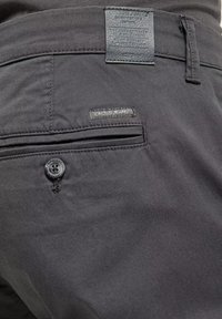 Czarne dżinsy z tylną kieszenią z zapięciem na guzik oraz skórzaną metką. Gładka faktura z delikatnymi detalami szycia.