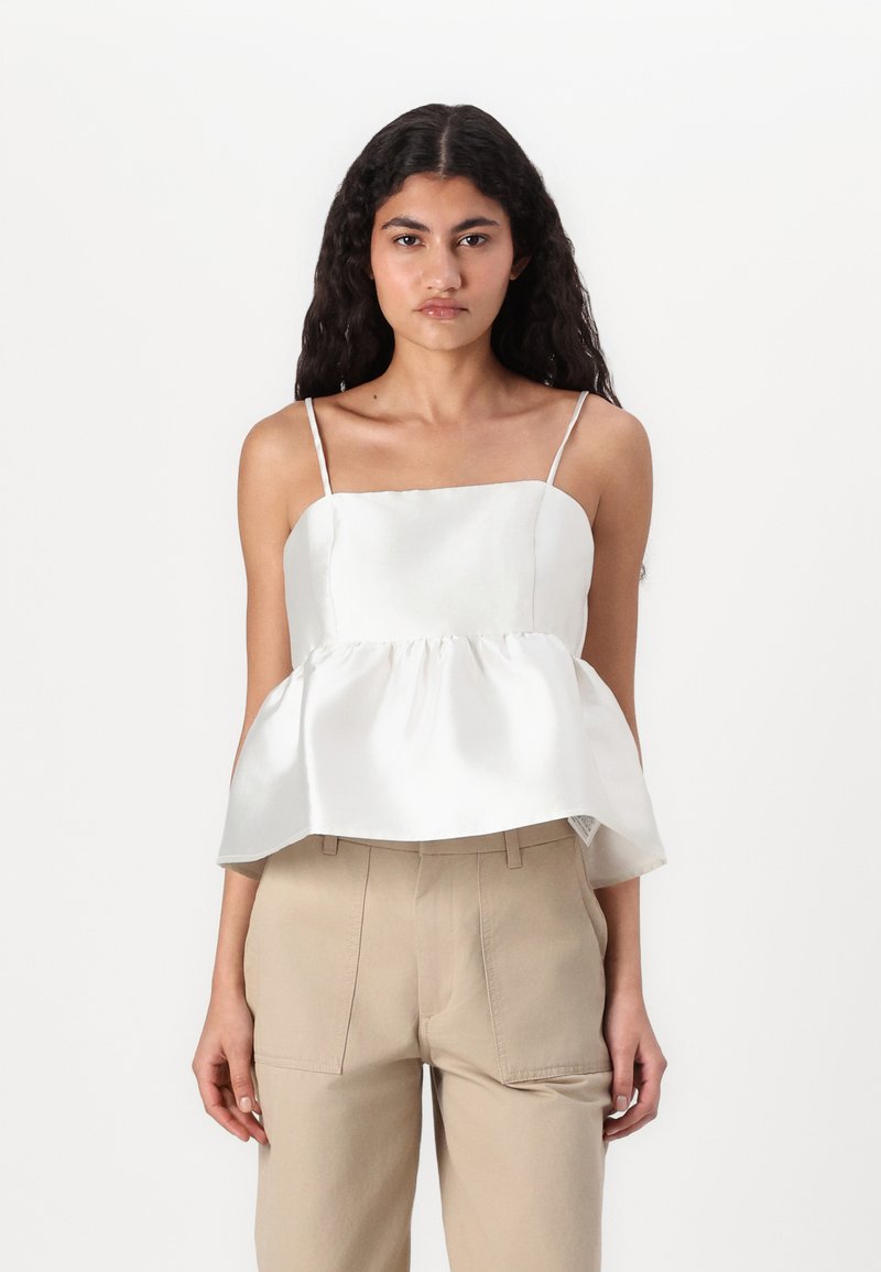Hvit sateng peplum-top med firkantet halslinje og tynne spaghettistropper, kombinert med beige høyt liv-bukser med sidelommer.