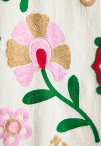 Textile with embroidered flowers in pink, beige, red, and green thread on a cream fabric background.