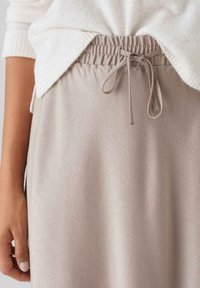 Helle beigefarbene Skirt mit weicher Textur, elastischem Bund und Kordelzugdetails. Kombiniert mit einem cremefarbenen Pullover.