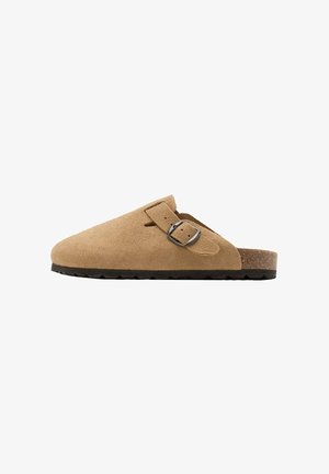 Sabot en daim marron clair à enfiler avec une bride noire à boucle, semelle intérieure en liège et semelle extérieure noire texturée, présenté de profil sur fond blanc.