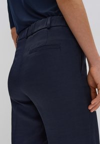 Pantalons bleu marine en tissu doux et lisse, avec une taille élastique et une poche arrière unique. Ils présentent une coupe décontractée et des lignes épurées.