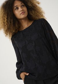 Blusa nera con ricami floreali, scollo rotondo, maniche lunghe e materiale trasparente. La texture morbida valorizza il design intricato.