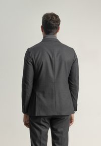 Chaqueta de traje ajustada en color gris oscuro con un cuello estrecho, que presenta una textura suave y detalles de costura sutiles, mostrada desde la parte posterior.