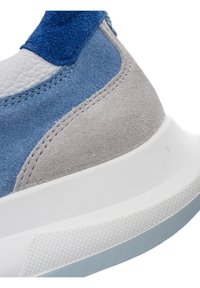 Gros plan sur le talon d'une basket en daim bleu, gris et blanc avec une semelle en caoutchouc blanche texturée et des coutures détaillées.