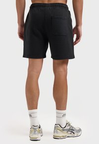 Zwarte shorts van zacht materiaal met een elastische tailleband en een enkele achterzak. Knie-lange pasvorm met een losse fit.