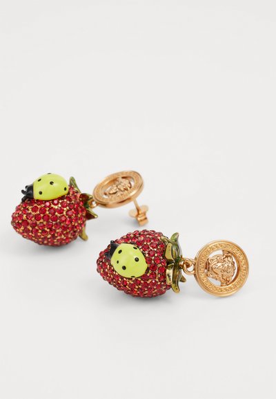 Red strawberry-shaped earrings adorned with sparkling red gems, green accents, and a gold-tone backing featuring a logo medallion.