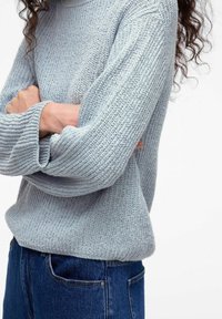 Jasnoniebieski sweter z dzianiny o ribbowym wzorze i długich rękawach, w połączeniu z ciemnoniebieskimi dżinsami. Tkanina charakteryzuje się luźnym splotem.