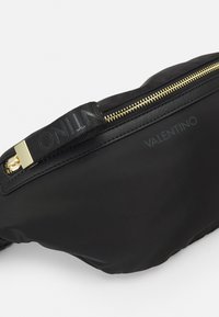 Svart bältesväska i nylon med en guldfärgad dragkedja och en strukturerad rem med "VALENTINO"-logotyp. Slät yta med rundade kanter.